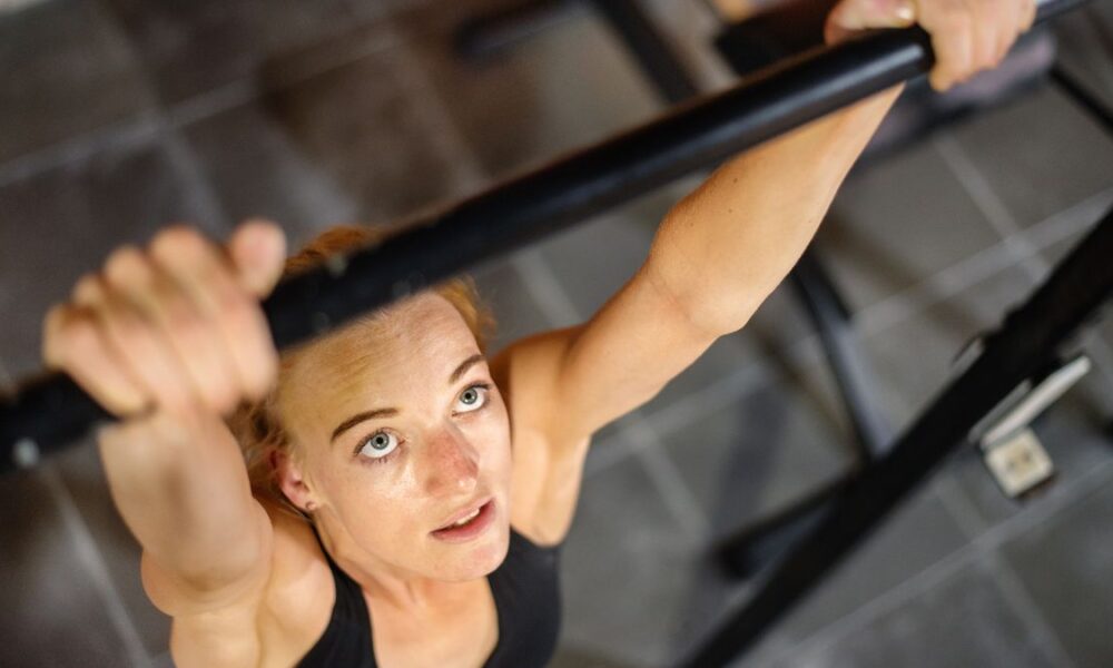 Woman gripping pull-up bar and looking up at it