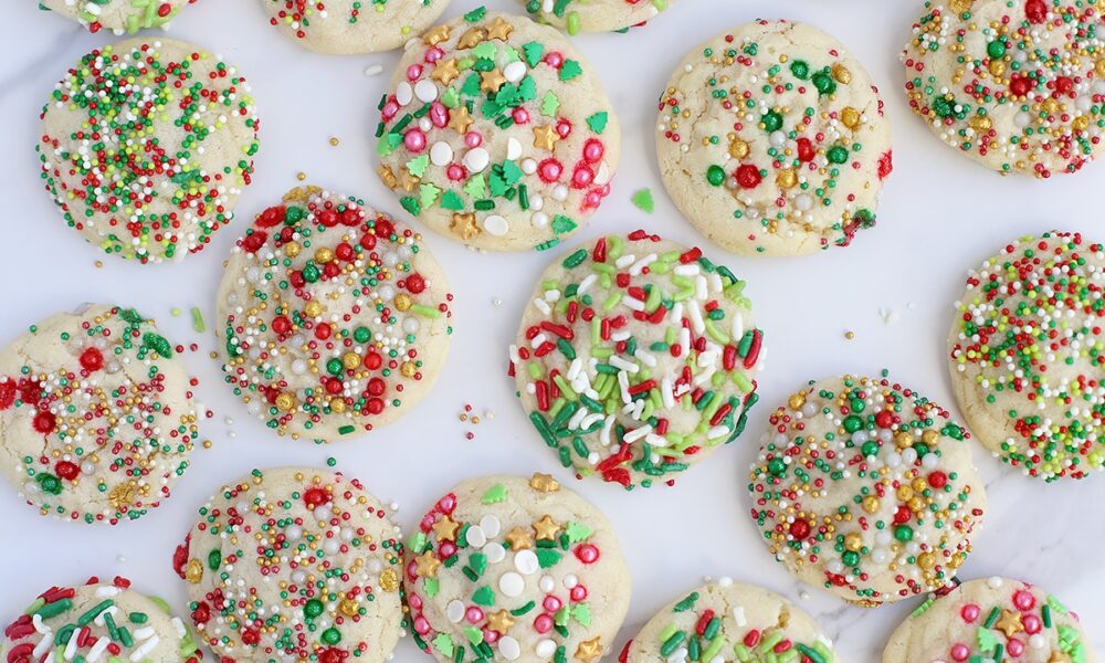 Holiday sugar cookies topped with colorful sprinkles spread out on a marble countertop.