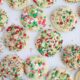 Holiday sugar cookies topped with colorful sprinkles spread out on a marble countertop.