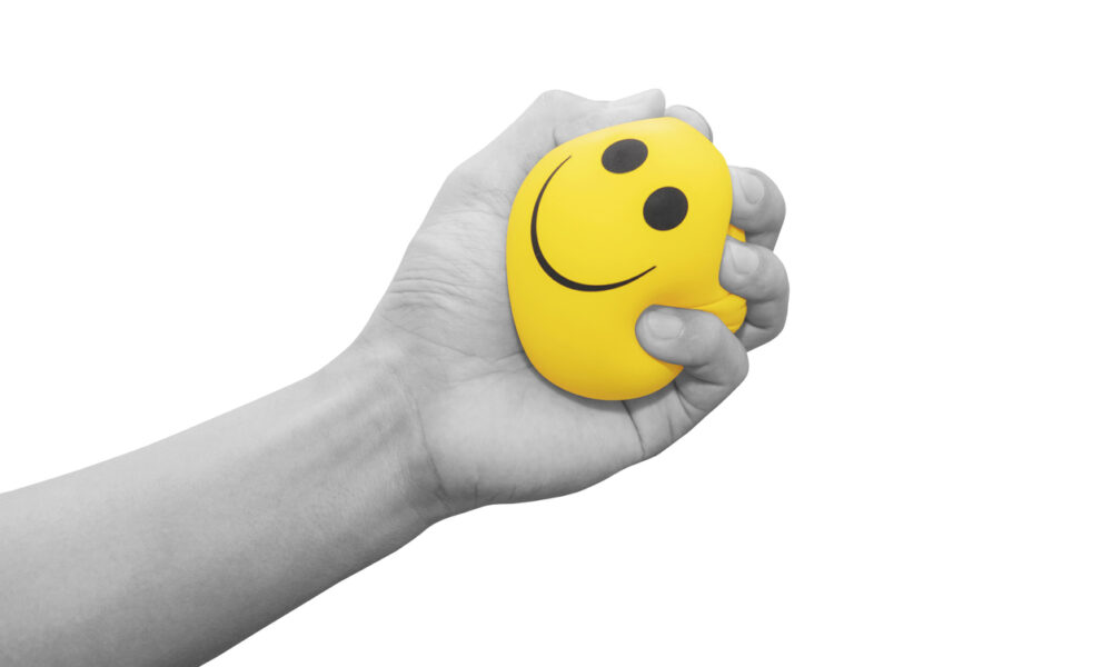 hand squeezing a stress ball with a smiley face on it