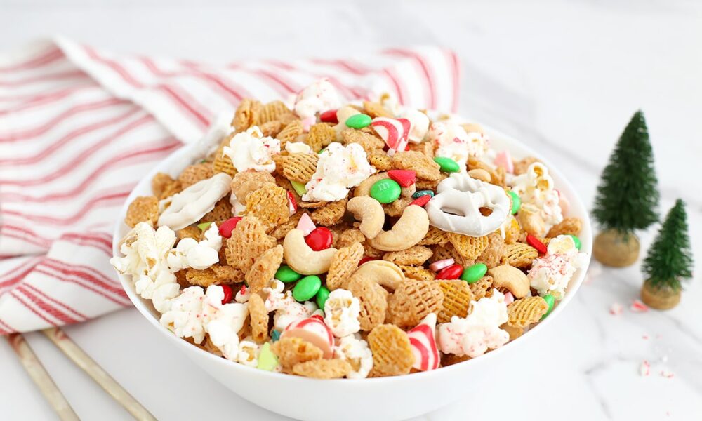 A bowl filled with holiday snack mix with a red and white striped linen and mini christmas trees in the background.