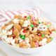 A bowl filled with holiday snack mix with a red and white striped linen and mini christmas trees in the background.