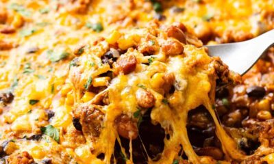 A skillet with melted cheese being lifted, revealing a cheesy, bean and meat mixture beneath.