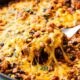 A skillet with melted cheese being lifted, revealing a cheesy, bean and meat mixture beneath.