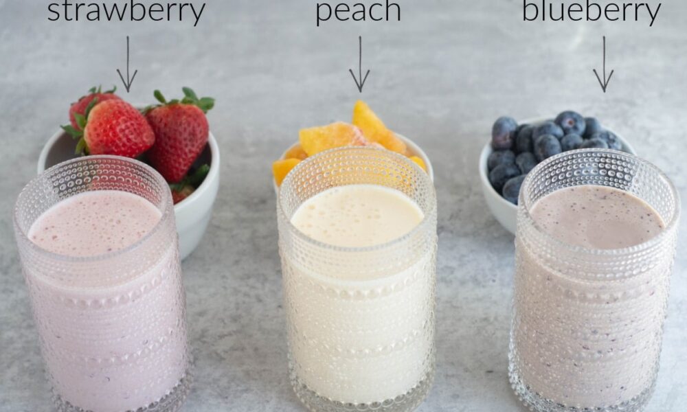 Glasses of drinkable yogurt sit in front of the fresh fruit that's in them: strawberries, peaches, and blueberries.