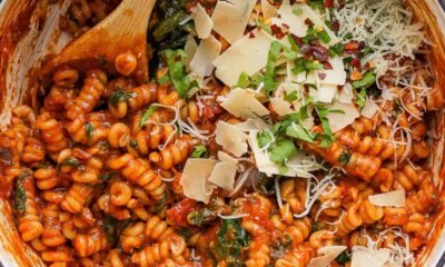 A pot of tomato-based pasta with spinach, garnished with grated cheese and herbs.