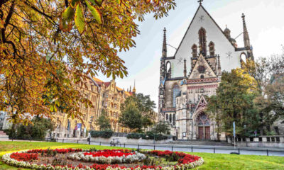 A historic church with a large, ornate entrance sits behind a circular garden with colorful flowers and vibrant autumn foliage.