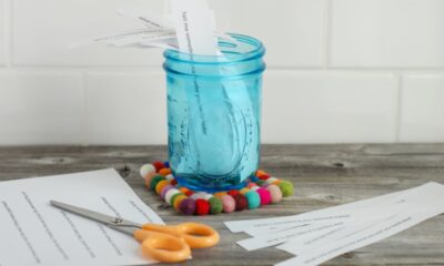 A blue jar of conversation starters sits on a wood table alongside a pair of scissors and slips of paper.