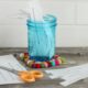 A blue jar of conversation starters sits on a wood table alongside a pair of scissors and slips of paper.