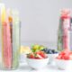 Two glass jars of homemade fruit popsicles sit on a counter alongside small white dishes of fruit.