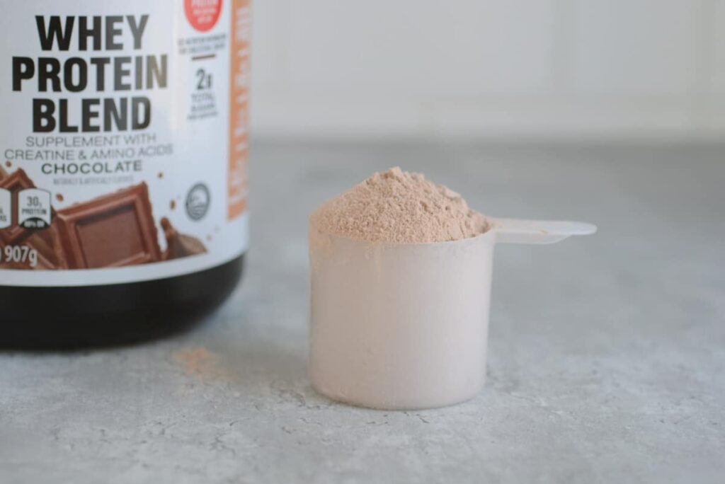 A scoop of chocolate protein powder sits next to a tub of protein powder