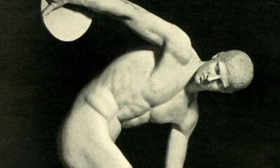 Black-and-white photo of a discus thrower sculpted in ancient Greek style, depicting a muscular male figure in mid-throw, symbolizing principles of physical fitness.