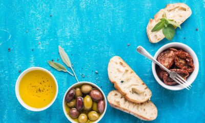 Mediterranean snacks set. Olives, oil, sun-dried tomatoes, herbs and sliced ciabatta bread on over blue painted background, top view, copy space