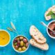 Mediterranean snacks set. Olives, oil, sun-dried tomatoes, herbs and sliced ciabatta bread on over blue painted background, top view, copy space