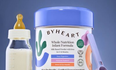 ByHeart infant formula can on a blue background with a bottle and scoop next to it.