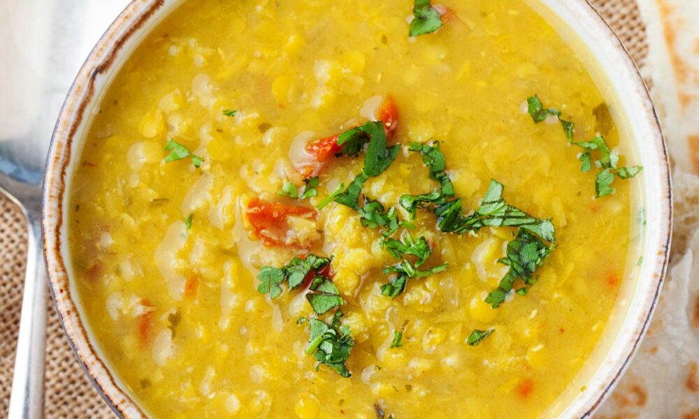 Slow cooker dal served in a white bowl, garnished with cilantro, with naan on the side.