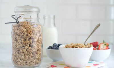 A jar of homemade granola sits next to a bowl of it, plus bowls of blueberries and strawberries