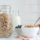 A jar of homemade granola sits next to a bowl of it, plus bowls of blueberries and strawberries