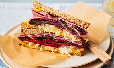 Slimming World New York deli-style salt beef and mustard sandwich. The sandwich is made up of two slices of wholemeal bread filled with beef, sauerkraut and marinated beetroot. It sits on light brown baking parchment on top of a white plate. The background is light grey.