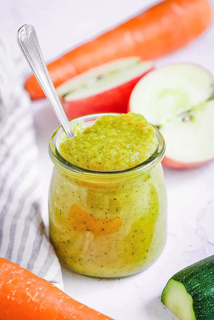 Zucchini baby food puree in a glass jar with a spoon.