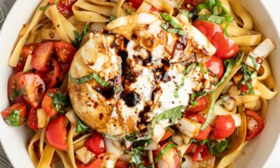 A bowl of pasta with tomatoes, fresh basil, and a large mozzarella ball drizzled with balsamic glaze.