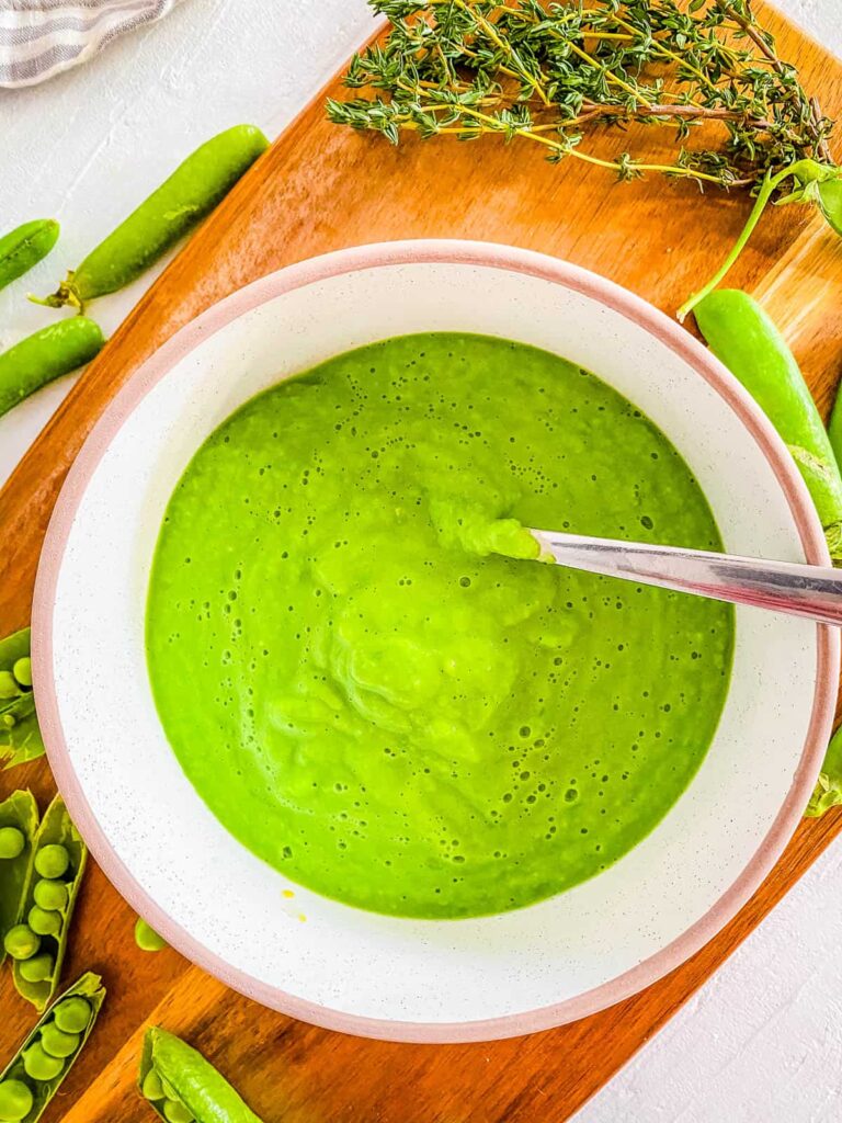 Baby food with peas in a white bowl with a spoon.