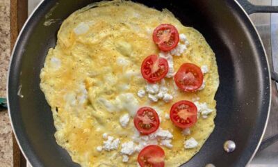 crepe style omelet in nonstick pan with feta cheese and tomatoes spread over half