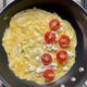 crepe style omelet in nonstick pan with feta cheese and tomatoes spread over half