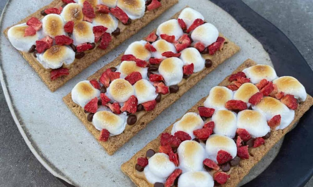 Three open-faced peanut butter and jelly s'mores dessert crackers on white ceramic serving platter.