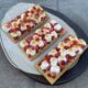 Three open-faced peanut butter and jelly s'mores dessert crackers on white ceramic serving platter.