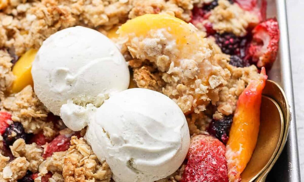 A dessert tray with fruit crisp topped with two scoops of vanilla ice cream and a spoon on the right side.