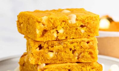 Three slices of golden yellow pumpkin blondies stacked on a plate, surrounded by white chocolate chips.