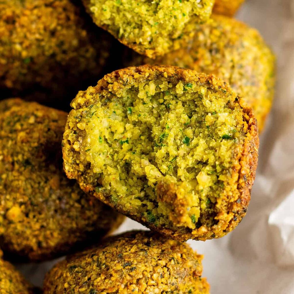 Close-up of a halved falafel, revealing its green, crispy interior. Other whole falafel pieces arrange in the background on parchment paper.