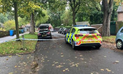 A police car parked across the road with blue police tape strung across the crime scene