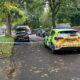 A police car parked across the road with blue police tape strung across the crime scene