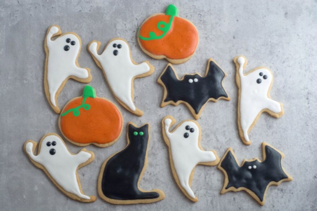 Whole wheat Halloween cookies in shapes of ghosts, cats, bats, and pumpkins sit on a gray counter.