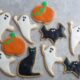 Whole wheat Halloween cookies in shapes of ghosts, cats, bats, and pumpkins sit on a gray counter.